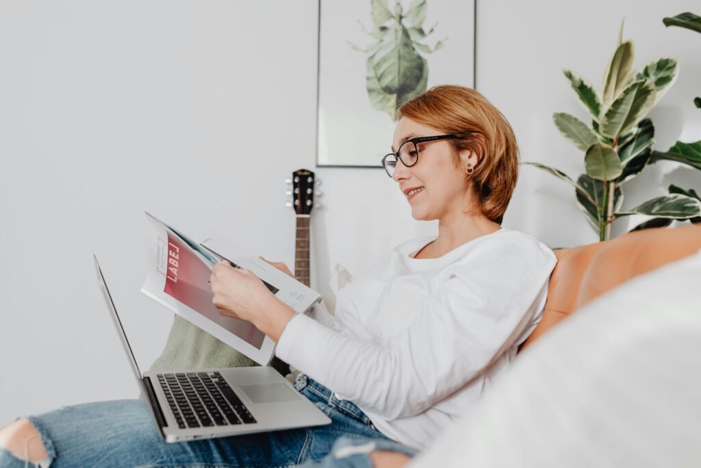 Woman reading a book at home while working on laptop – Daily habit for personal growth and self development